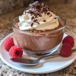 Chocolate mousse in a glass cup topped with whipped topping and chocolate shavings with berries on the side