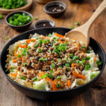 Skillet of egg roll in a bowl with ground meat, shredded cabbage, carrots, green onions, and sesame seeds.