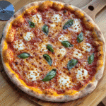 Homemade pizza with golden bubbly crust, melted cheese, and basil on a wooden peel.