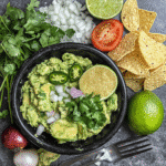 Overhead ingredients for authentic guacamole including avocados, lime, onion, cilantro, tomato, jalapeño, and salt