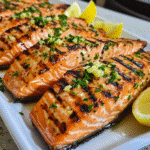 Grilled salmon fillets with grill marks, herbs, and lemon wedges