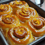Orange sweet rolls with orange glaze drizzled on top in a baking dish